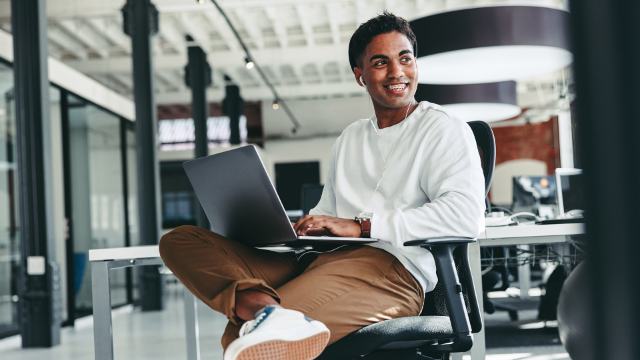 a well dressed casual man with braces and earbuds using a laptop in a modern office space