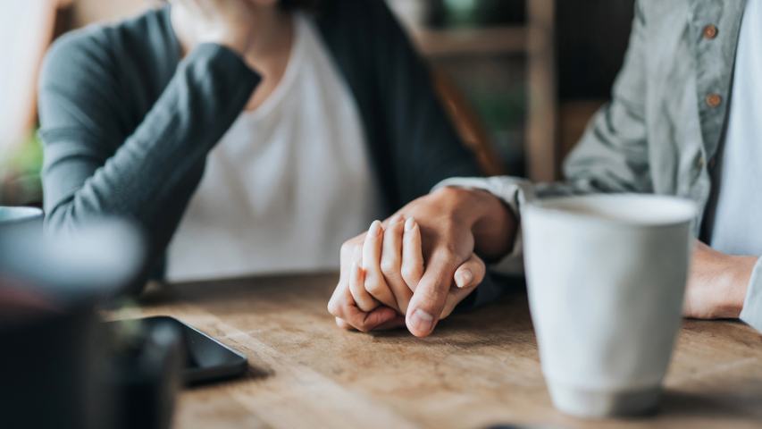 close up on woman and man holding hands at a cafe