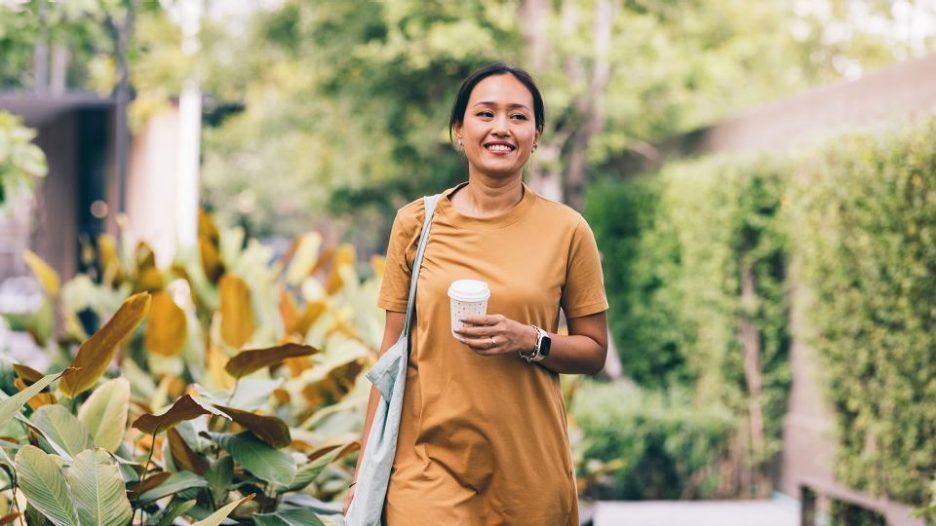 Smiling female walking in garden area caring takeaway coffee cup