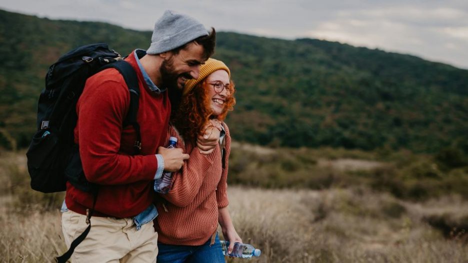 happy couple wearing beanies and carrying water bottles on a nature walk together