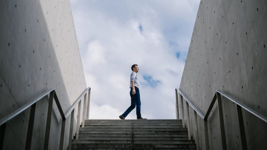 Business man walking outside above stairs with concrete walls on either side