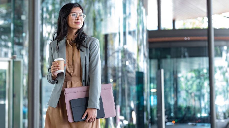 A professional woman looking at her phone while standing near the glass doors of a modern space