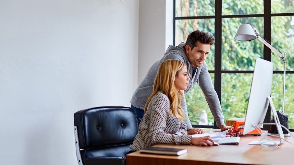 Young professional team of male and females in meeting on sofa in colourful modern office environment