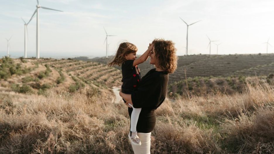 Lttle happy daughter gently touches mother on walk in nature. Rocky landscape and windmills in background. Happy family together.