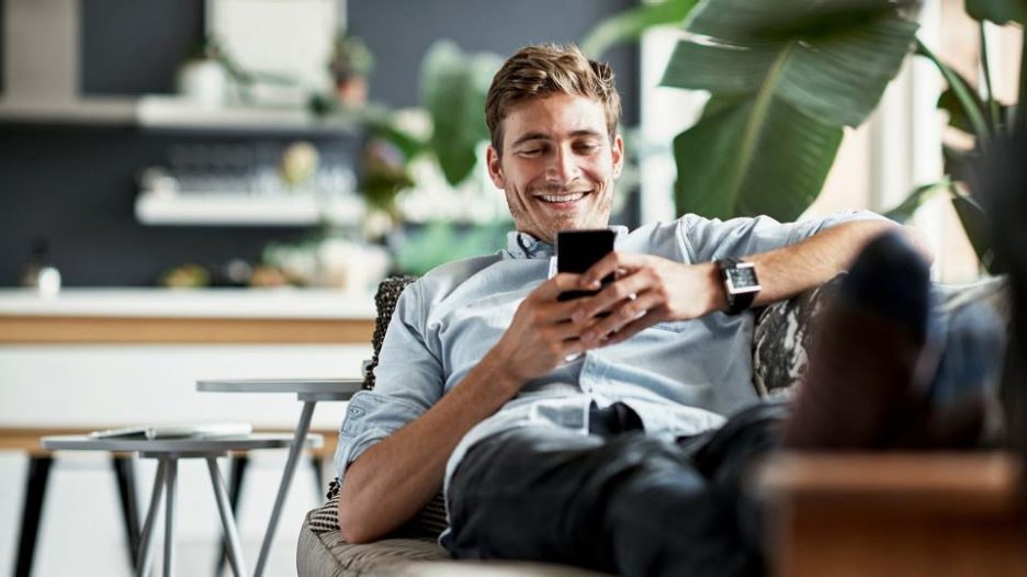 smiling man relaxing at home after work and using his phone