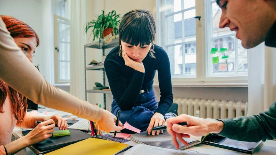 four colleagues at a desk in an office brainstorming together