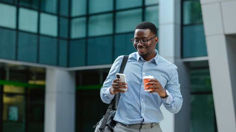 young african male drinking coffee and looking at his phone on the way to work