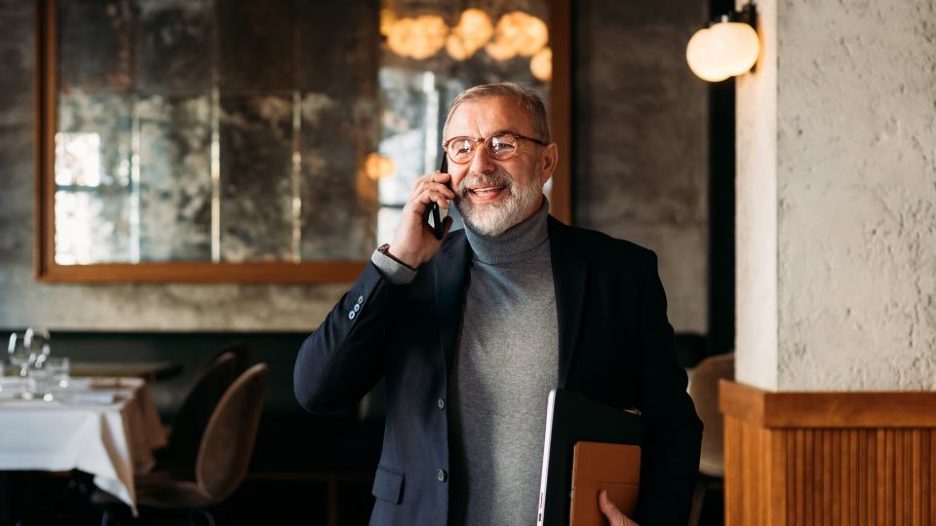 senior businessman standing in restaurant, talking on phone