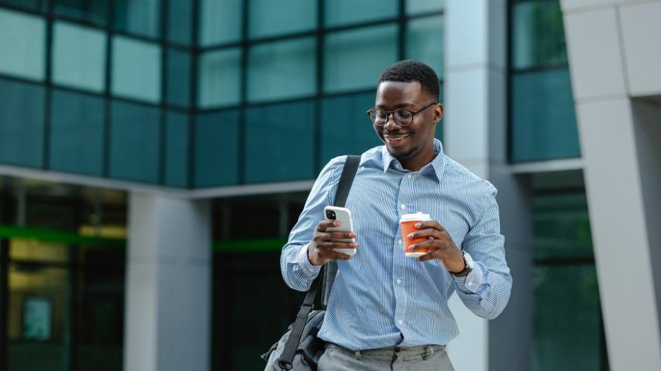 Young African-American businessman using a smart phone on the street. He is holding coffee to go and checking smart phone