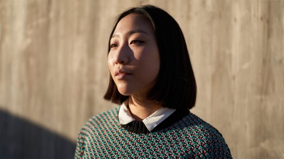 portrait of confident woman in casual clothes looking away while standing near wall on sunny day on city street
