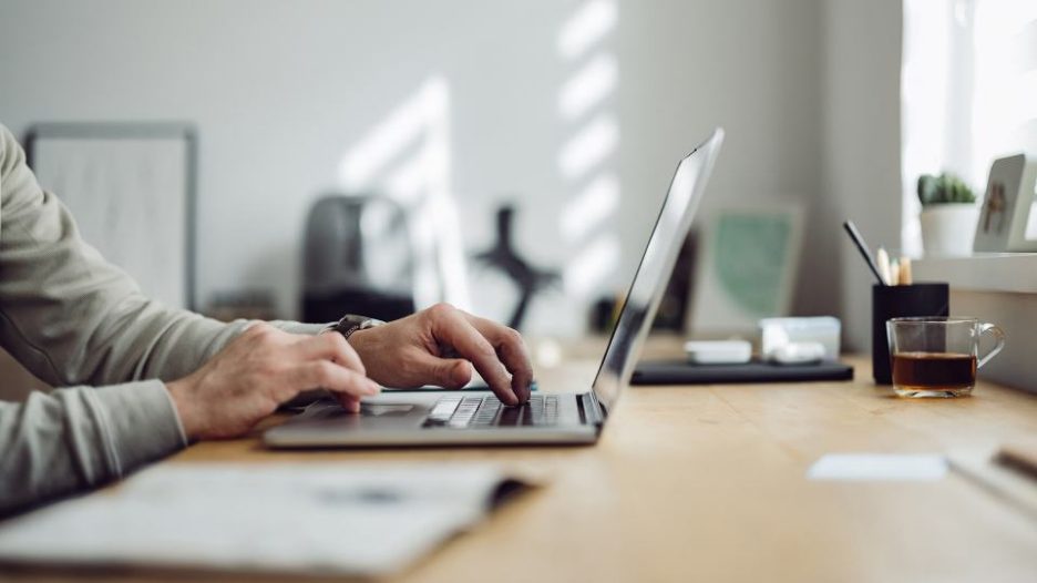 close up of a man's hands on his laptop in his home office 