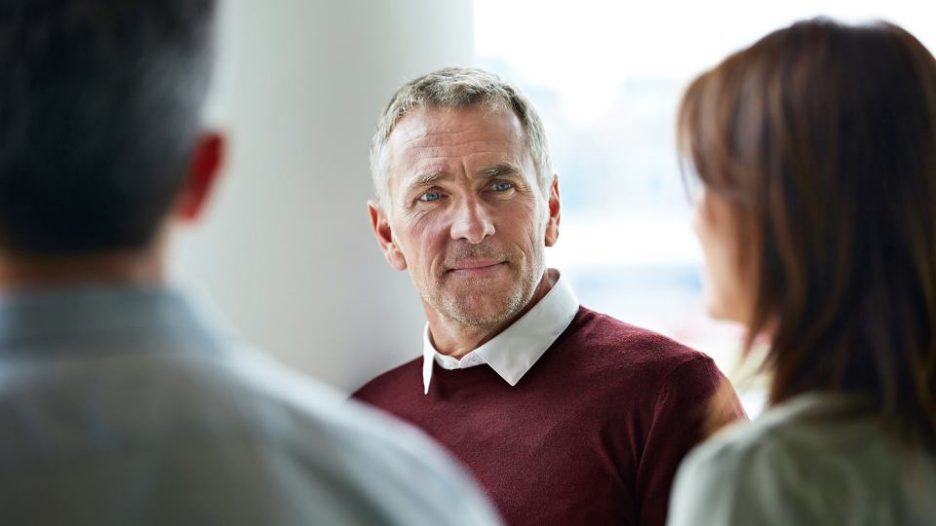 a professional man is listening carefully while his female colleague speaks and another man listens in