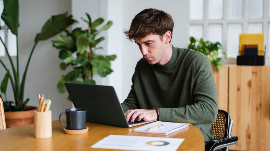 businessman working on business project using laptop and taking notes sitting in modern office full of plants