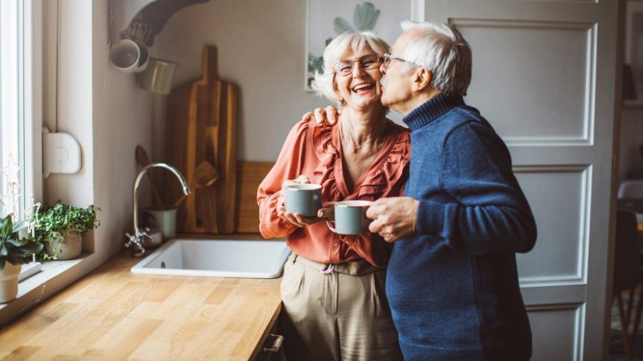 mature couple ejoying coffee and a kiss on the cheek in their kitchen