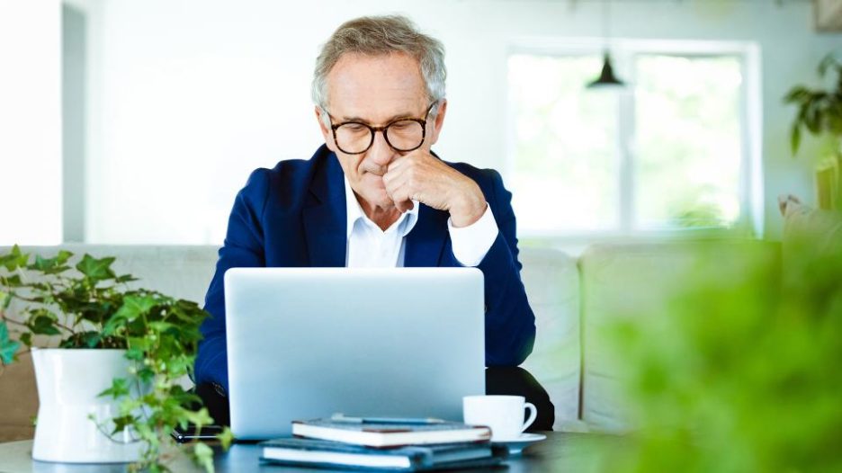 professional man thoughtfully looking at his laptop in a light filled modern office with plants