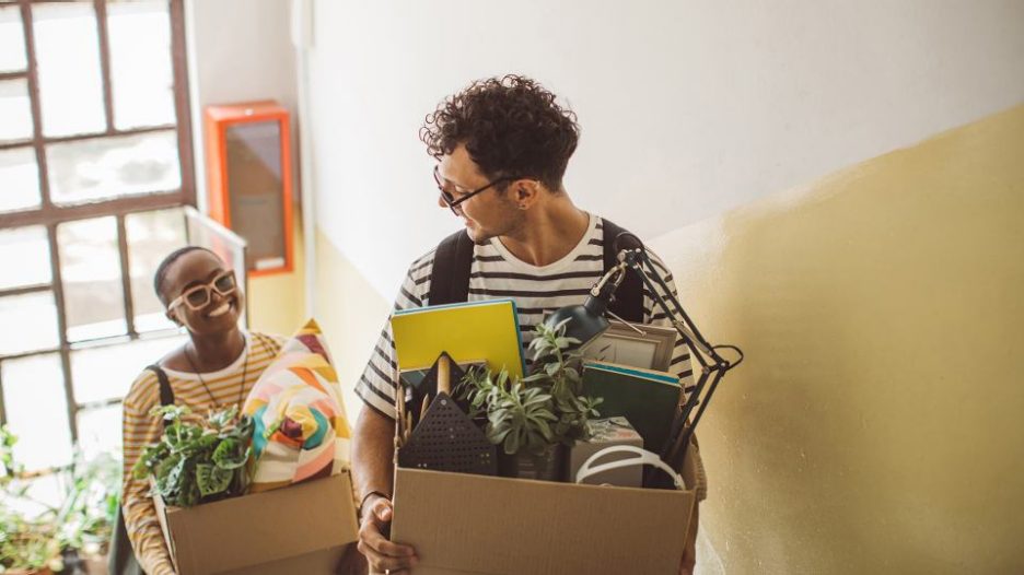 male and female friends in striped tee shirts carrying boxes of possessions upstairs