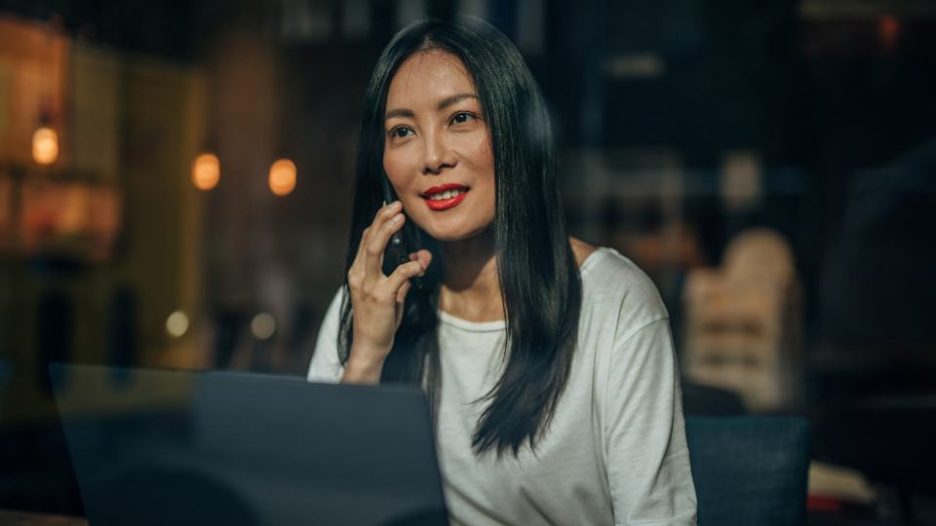 a woman is seen through a window at night, talking on her phone in front of a laptop