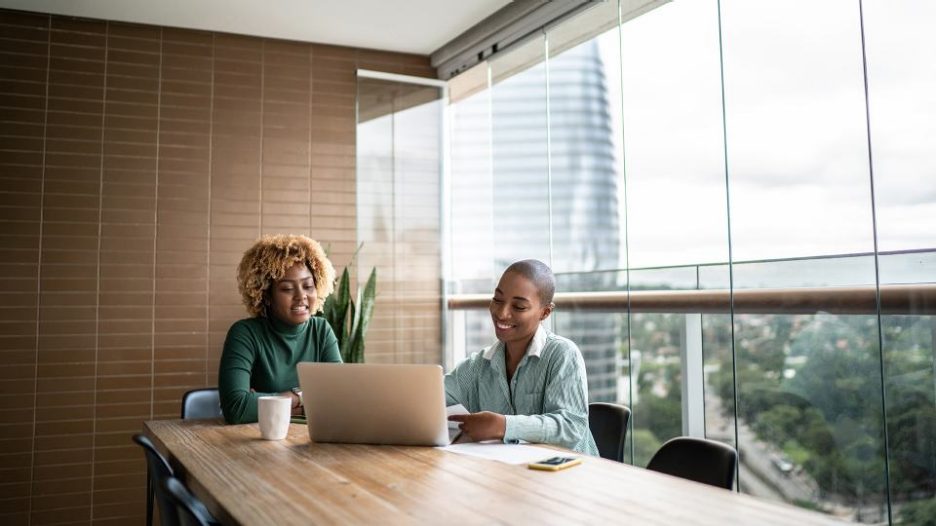 two women in a conference room with a laptop sitting near a window