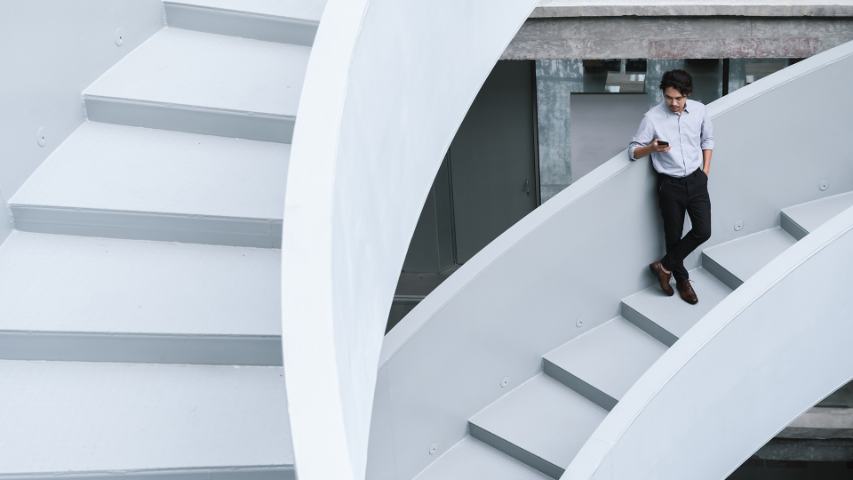 Young Asian businessman using smartphone on curving white stairs