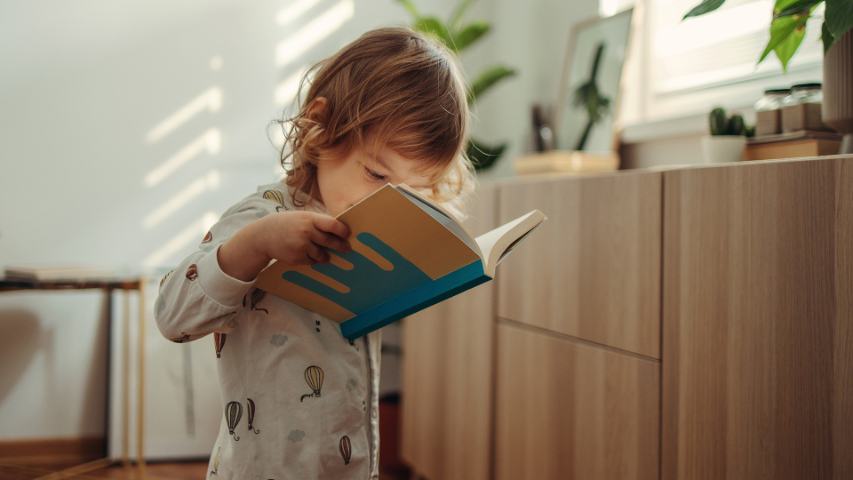 young child in pyjamas looking closely at a book in her room