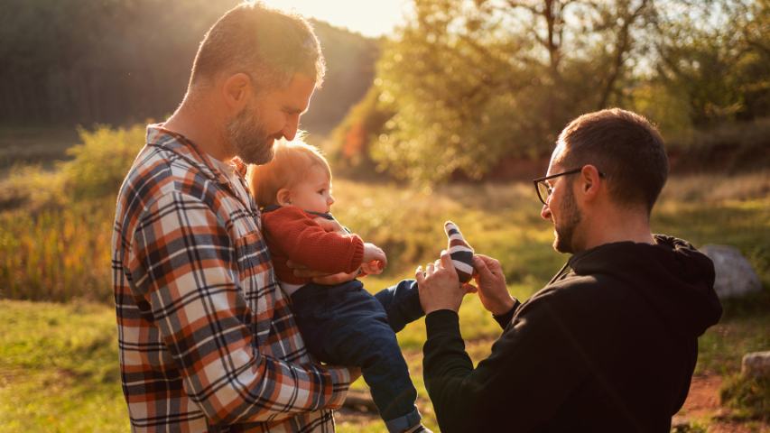 two happy loving men with a toddler outside in the late afternoon sun