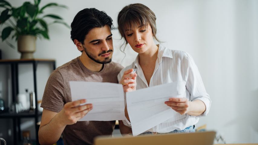 man and woman sitting slose together to compare paperwork with a laptop nearby