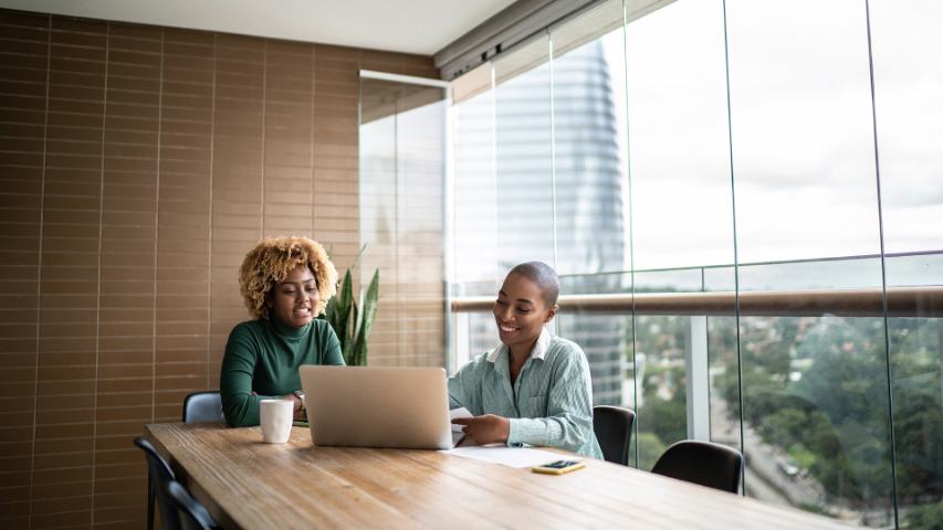 two women in a conference room with a laptop sitting near a window