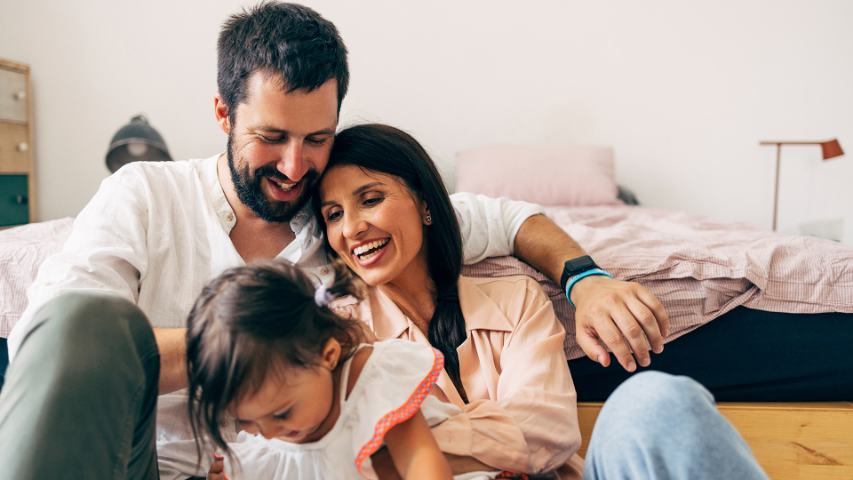 smiling mother and father with their young child in their bedroom at home