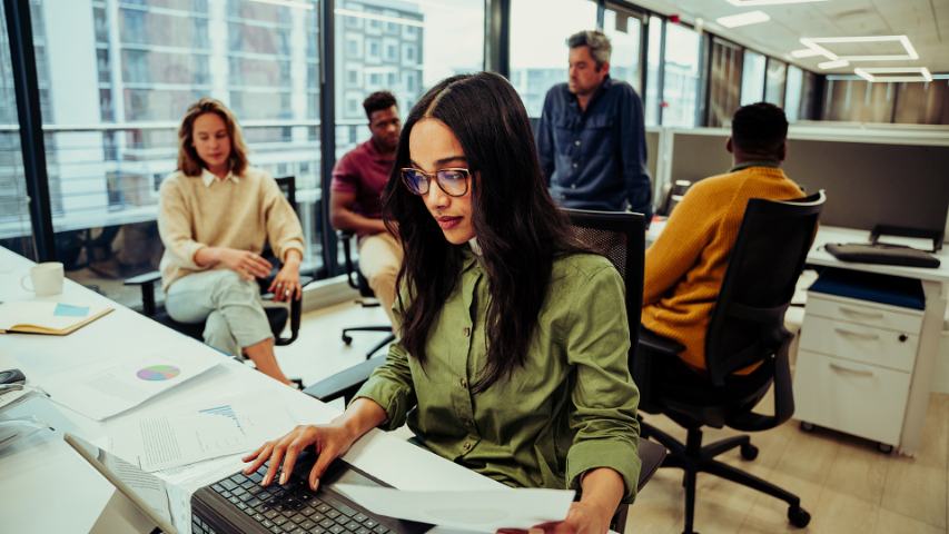 Young professional female focussed on laptop with colleagues sitting in background