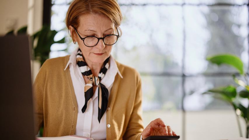 mature professional woman using a laptop and calculator in her office