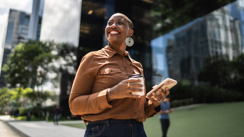 smiling professional woman outside an office building with coffee and a phone