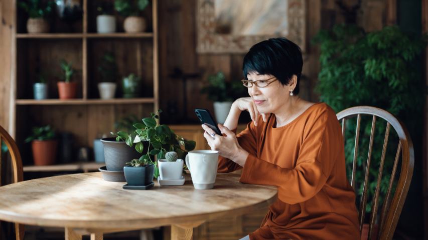 woman at home looking at her phone while drinking tea and surrounded by plants
