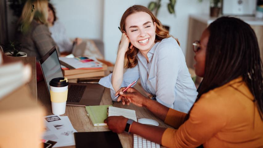 female colleauges chatting at desk in front of laptop