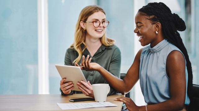 two women having a meeting and smiling while they look at a tablet