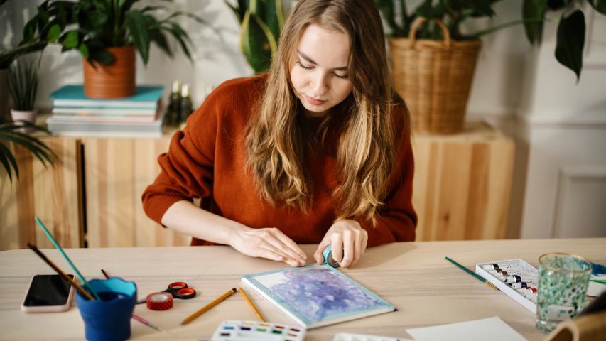 young woman doing watercolour art while sitting at a pine table