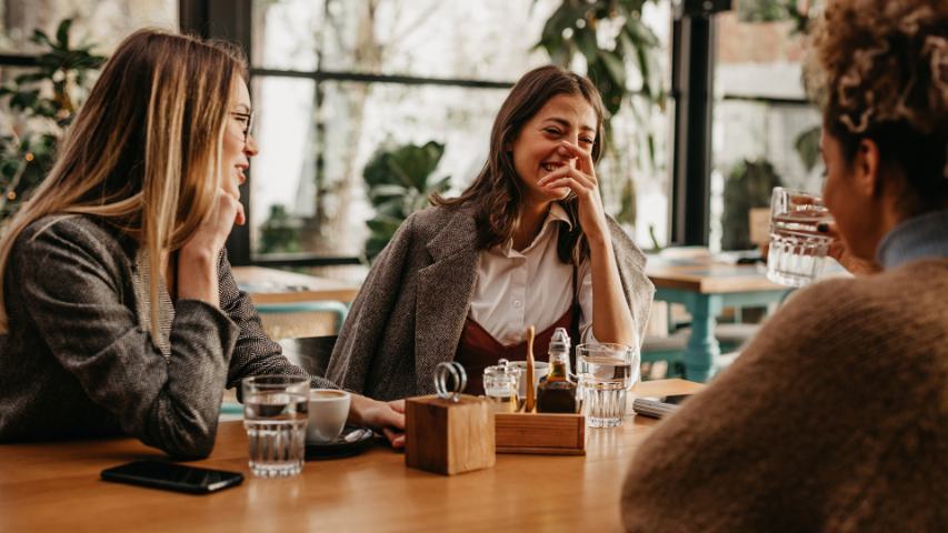 a group of three female friends laughing and enjoying time in a cafe