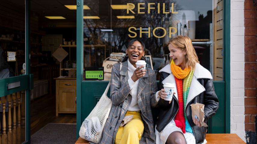 two femaile friends laughing as they sit outside a cafe with takeaway drinks