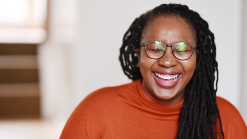 a woman in an orange top with glasses is laughing and closing her eyes