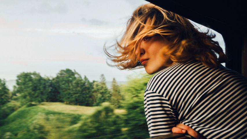 Female leaning out of moving vechicle window with hair blowing in the wind