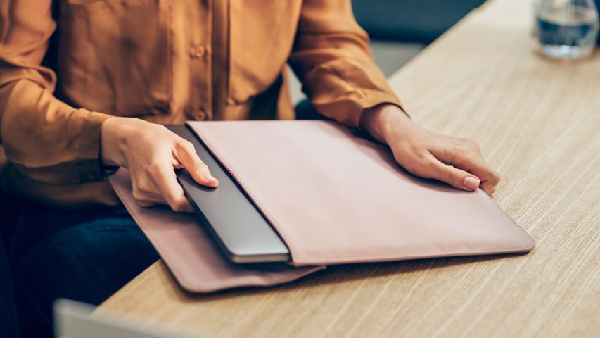 close up of a person in a burnt orange shirt removing aheir laptop from its case on a desk