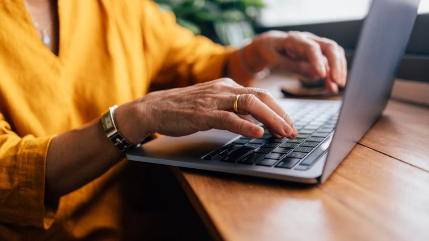 close up of a woman's hands typing on a laptop on a wooden table