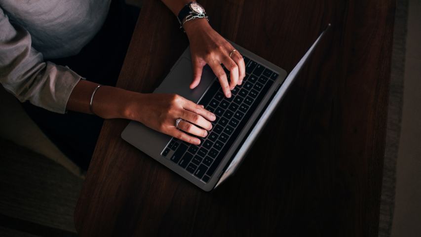 close up of a woman's hands typing on a laptop in low light