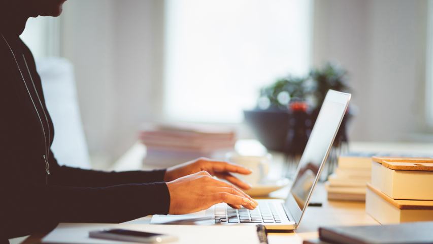 close up of a woman wearing black and typing on a laptop in a white office