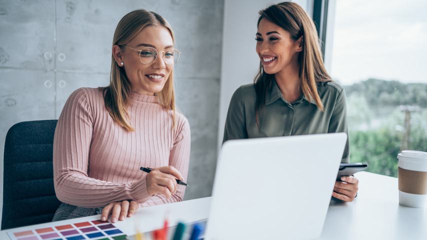 two female coworkers in a casual meeting with a laptop, colour swatches and coffee nearby