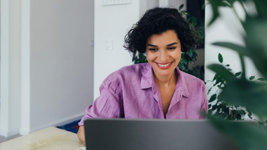 woman in a pink shirt is smiling at her laptop in an office setting