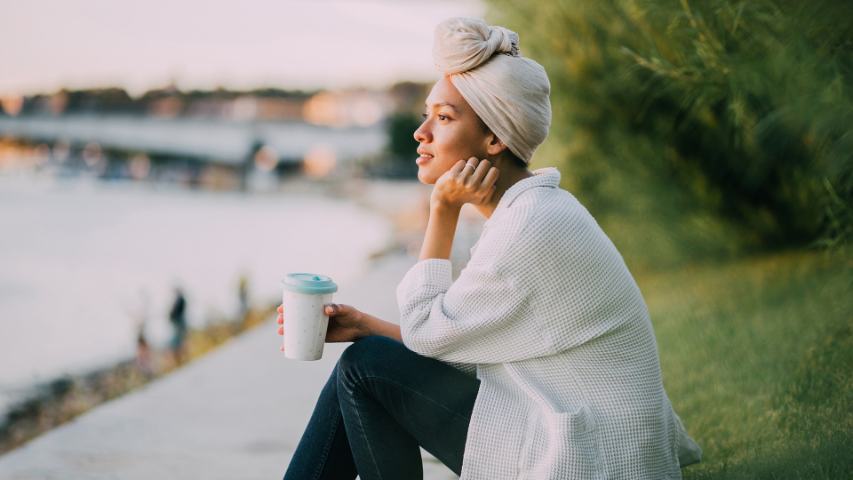 woman at a park with coffee looks hopefully across the water in the late afternoon