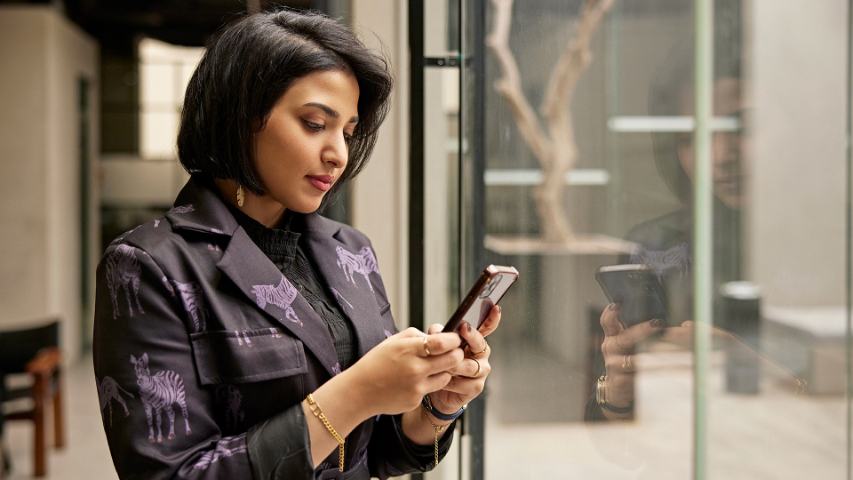 professional woman looking at her phone while standing near the glass doors of a modern space