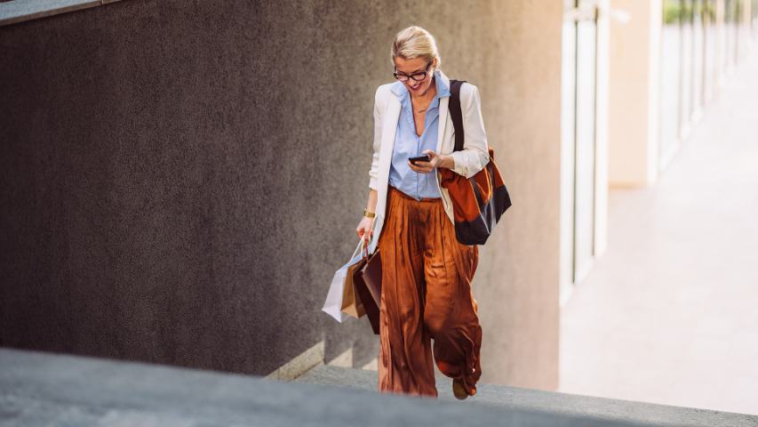 a well drssed woman with shopping bags is climbing stairs and smiling at her phone