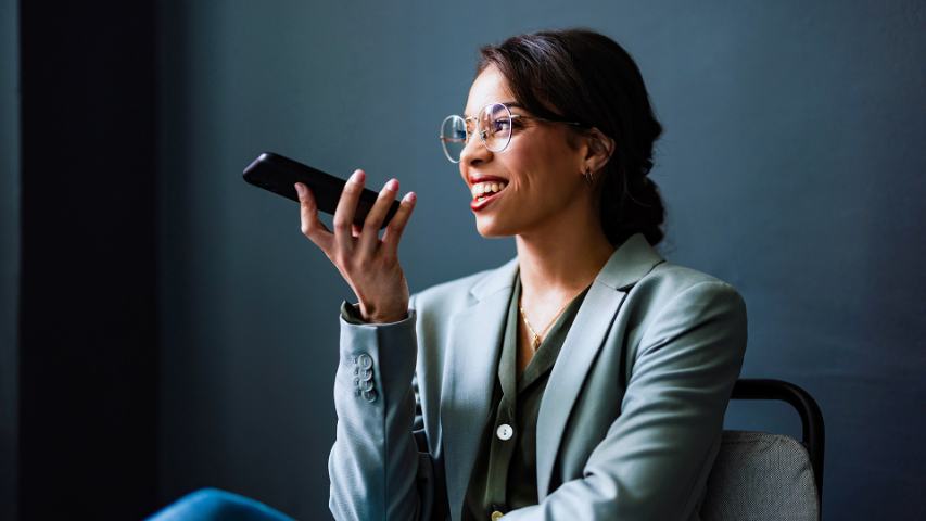 professional woman holds her phone and speaks into it with a dark blue wall and natural light