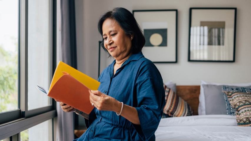 woman reading through documents while sitting on her bed near a window